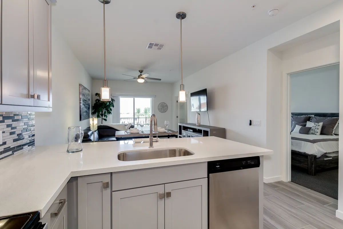 A modern kitchen with a central island, pendant lights, and a partial view into the living room. The space is designed for both cooking and socializing, with ample seating around the island and an inviting, cozy ambiance enhanced by warm lighting.