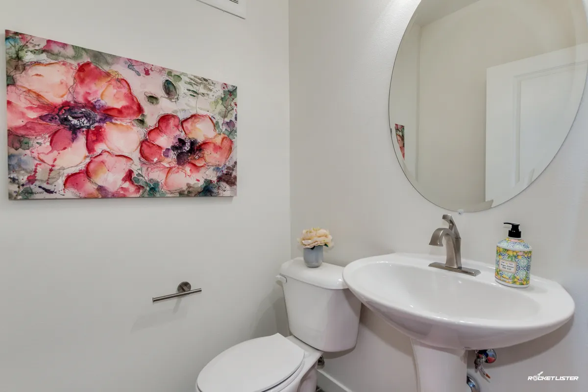 A compact, well-designed half bath featuring floral artwork, a circular mirror, a modern sink, toilet, and a small flower arrangement. The bright and cheerful décor makes it inviting for quick visits or freshening up.